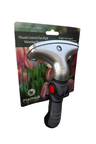 A packaged thumb control fan style watering nozzle with a black and silver color scheme, held in a hand against a background of construction and garden supplies.