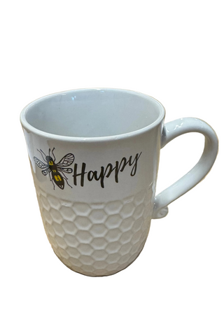 A white ceramic mug with a happy word and a bee illustration on it, placed on a table.