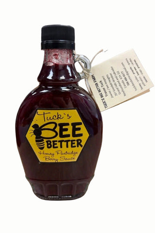 A bottle of Tuck's Bee Better Honey Patchwork Jelly Sauce on a light wood desk, with a handwritten tag attached.