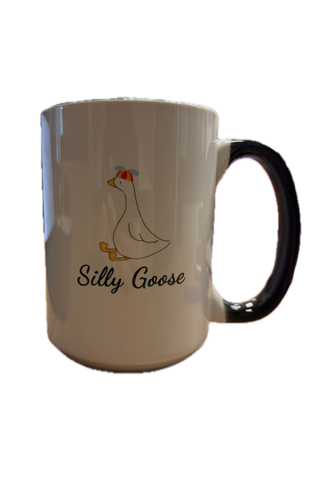 A white ceramic mug with a glossy black handle, featuring a cartoon illustration of a white goose with orange beak and feet, next to the text 'Silly Goose' in black script.