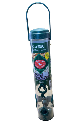 A clear, cylindrical bird feeder with a green top and a hanging mechanism, placed on a counter inside a store.
