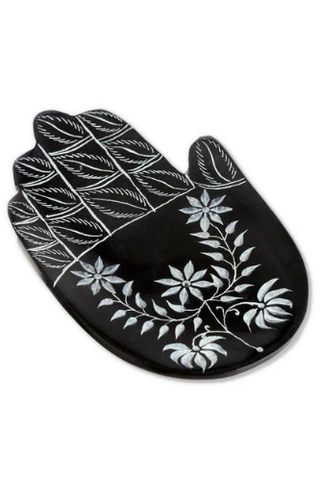A black incense holder in the shape of a hand with white floral patterns.
